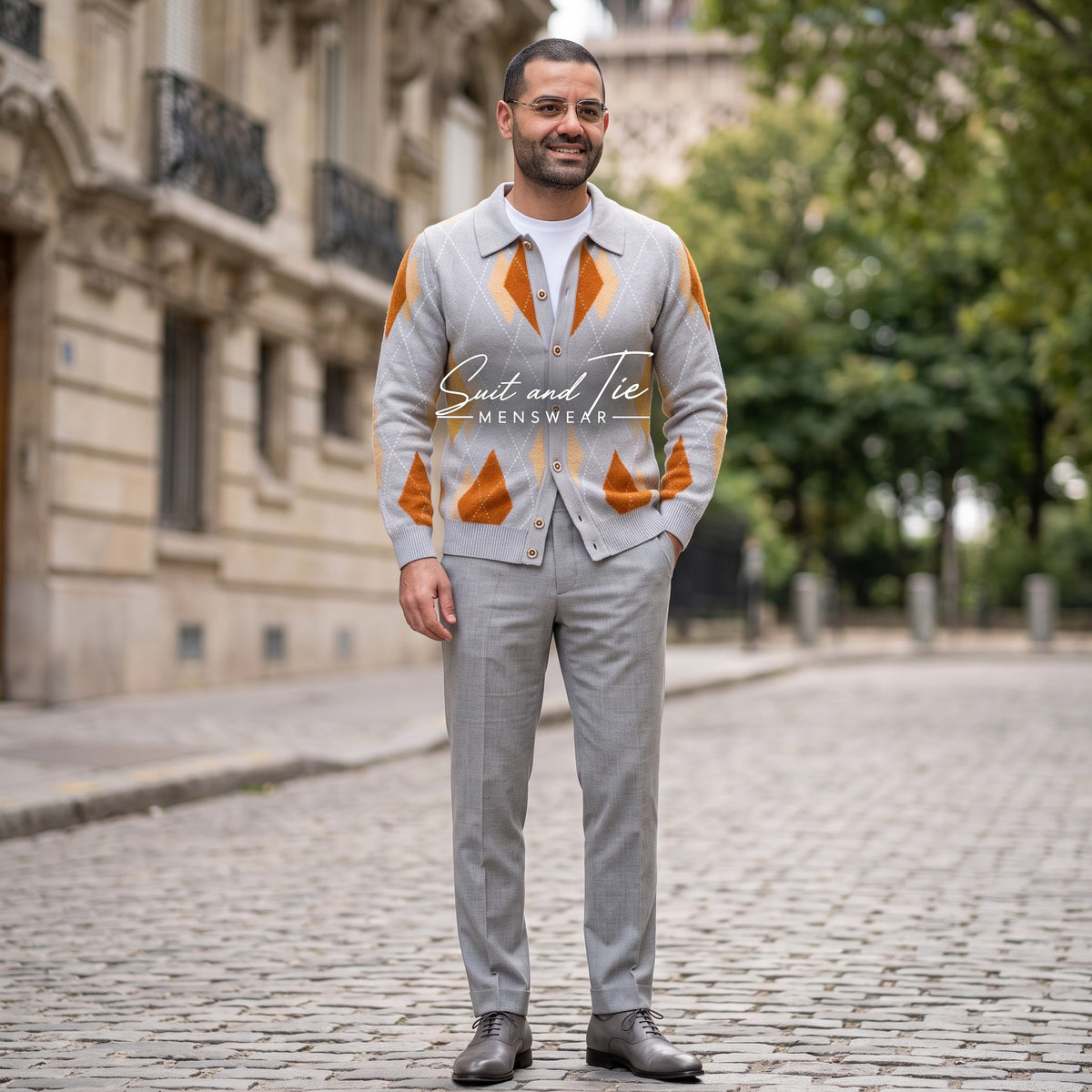 A man wearing A gray knit cardigan sweater with an orange and beige argyle pattern, featuring a button-down front, a pointed collar, and a visible 'Prestige' neck label. A large 'Suit and Tie Menswear' watermark is overlaid across the center.