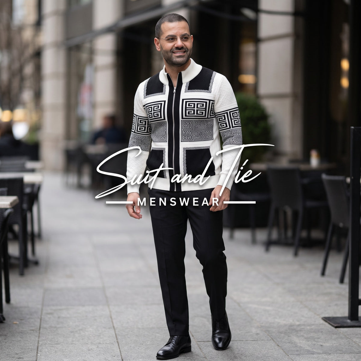 A man wearing a black and white patterned zip-up sweater, black trousers, and black dress shoes walks down a city sidewalk. A large 'Suit and Tie Menswear' watermark is overlaid across the center of the image.