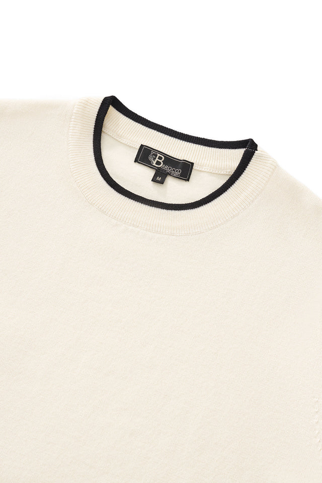 Close-up of a beige sweater with black trim and a brand label on a white background