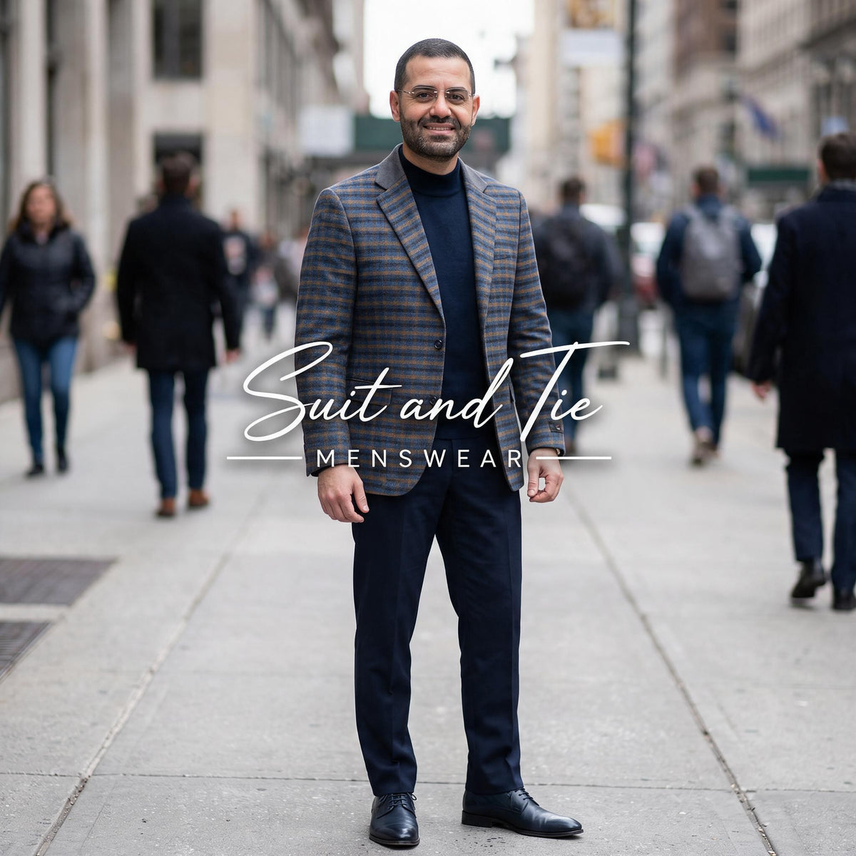 A man stands on a city sidewalk wearing a tailored plaid blazer and dark trousers, with a visible 'Suit and Tie Menswear' watermark across the center. Pedestrians are blurred in the background.