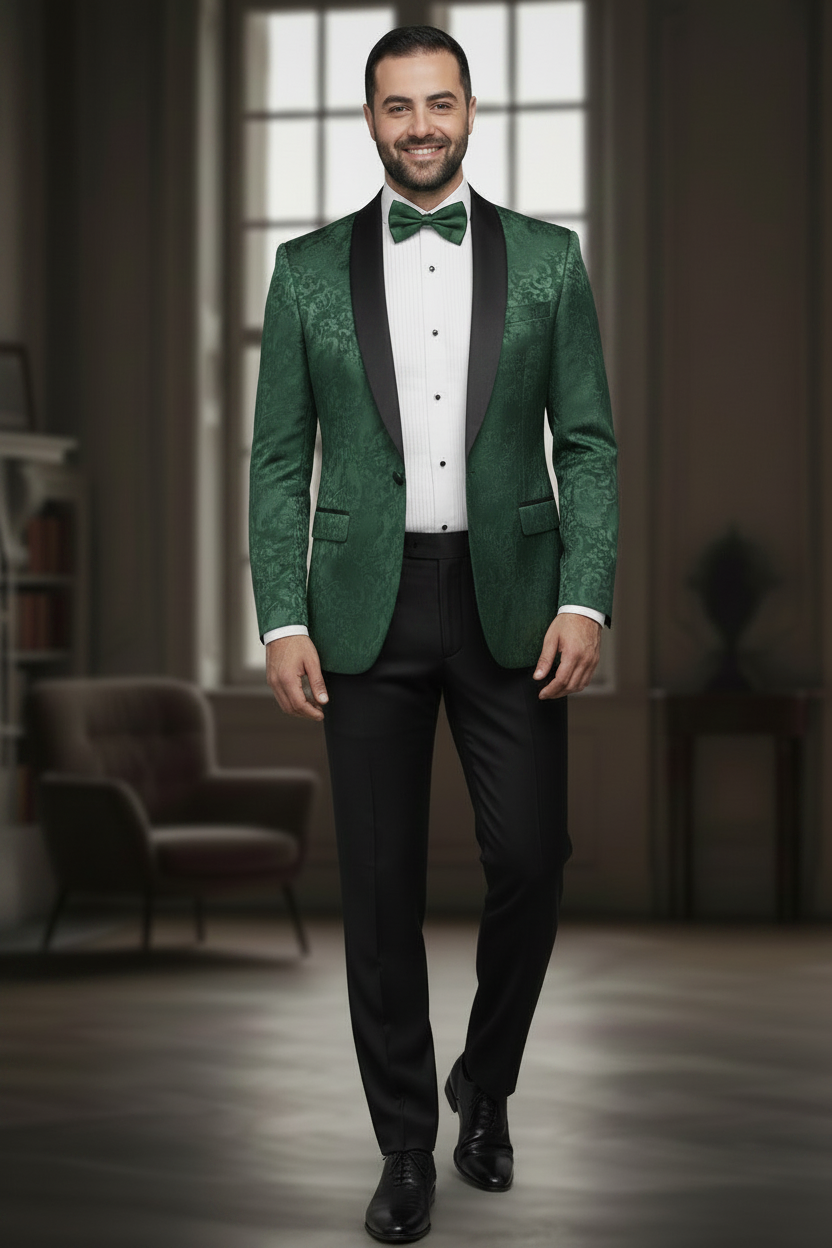 A man wearing a green patterned tuxedo jacket with black satin lapels, a white dress shirt, a green bow tie, and black trousers, standing in a dimly lit indoor setting.