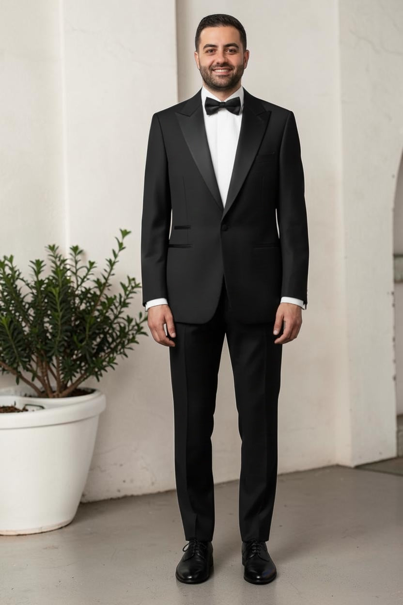 Man wearing a black tuxedo standing indoors with a plant in the background