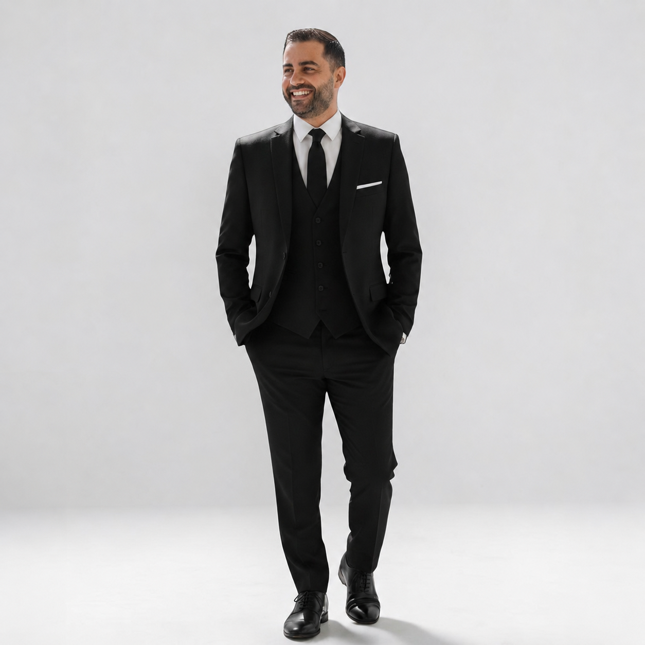 Man wearing a black suit with a white shirt and black tie on a light gray background